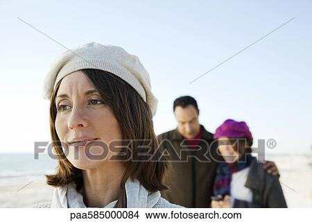 Picture - Woman looking away in thought, family in background. Fotosearch