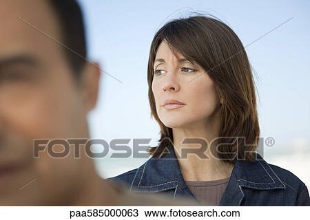 Stock Image - Woman looking away with furrowed brow, man in foreground. Fotosearch