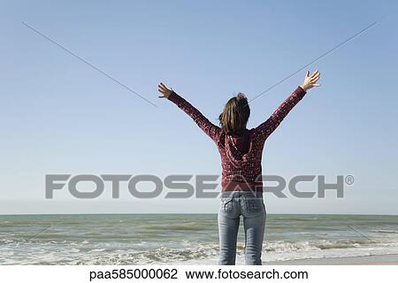 Woman standing on beach with arms raised View Large Photo Image Stock Image - Woman standing on beach with arms raised. Fotosearch