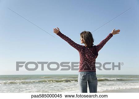 Stock Photography - Woman standing on beach with arms raised. Fotosearch