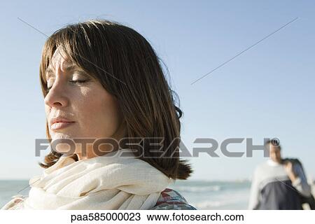 Stock Image - Woman standing on beach with eyes closed. Fotosearch