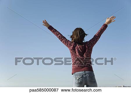 Stock Photo - Woman standing outdoors with arms raised in the air. Fotosearch