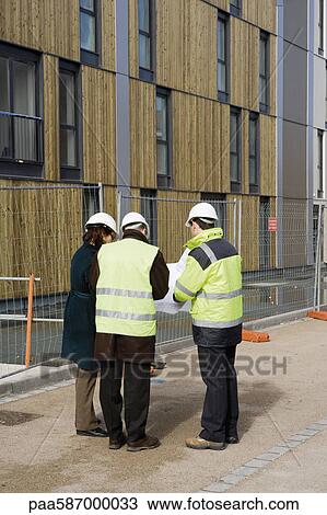 Stock Image - Building contractor and architects in discussion at construction site. Fotosearch