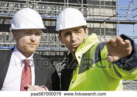 Stock Photo - Building contractor talking to businessman at construction site. Fotosearch