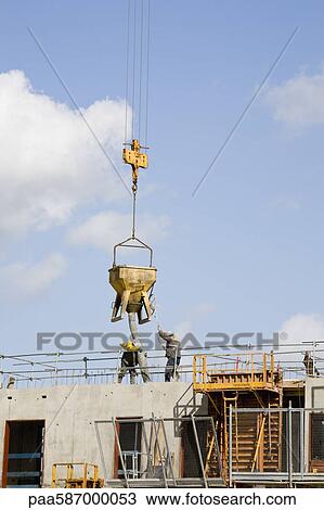 Construction workers guiding bucket suspended by crane to deposit concrete on building under construction View Large Photo Image Stock Image - Construction workers guiding bucket suspended by crane to deposit concrete on building under construction. Fotosearch