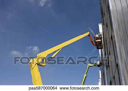 Picture - Construction workers in cherry picker bucket working on building exterior. Fotosearch