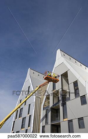 Stock Image - Construction workers in cherry picker bucket working on building exterior. Fotosearch