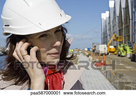 Stock Image - Female architect using cell phone at construction site, portrait. Fotosearch