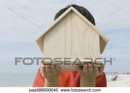 Stock Image - Boy holding wooden birdhouse in front of face. Fotosearch