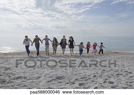 Stock Photograph - Group of people holding hands and running together on beach. Fotosearch