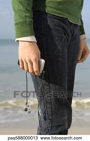 Stock Image - Person standing on beach, MP3 player in hand, cropped. Fotosearch