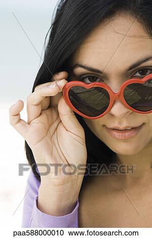 Woman lowering heart shaped sunglasses to look at camera, portrait View Large Photo Image Stock Image - Woman lowering heart shaped sunglasses to look at camera, portrait. Fotosearch