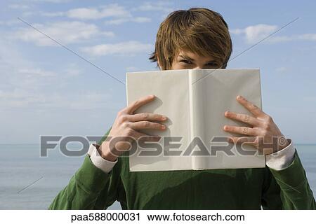 Young male holding book in front of face, portrait View Large Photo Image Stock Image - Young male holding book in front of face, portrait. Fotosearch
