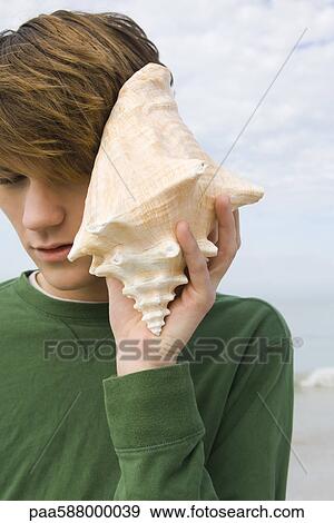Young male listening to conch shell View Large Photo Image Stock Photo - Young male listening to conch shell. Fotosearch