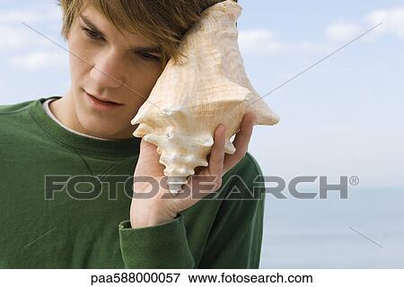 Stock Photo - Young male listening to conch shell. Fotosearch