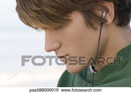 Young male listening to earphones outdoors View Large Photo Image Stock Photo - Young male listening to earphones outdoors. Fotosearch