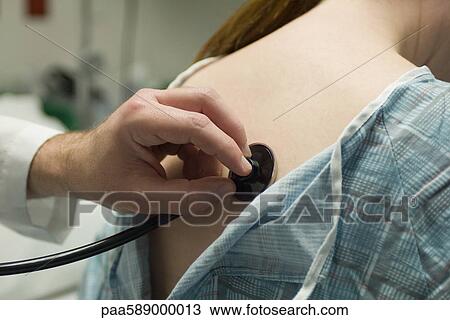 Stock Image - Doctor placing stethoscope on patient's back. Fotosearch
