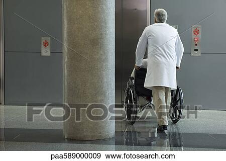 Doctor pushing patient in wheelchair toward elevator View Large Photo Image Stock Photo - Doctor pushing patient in wheelchair toward elevator. Fotosearch
