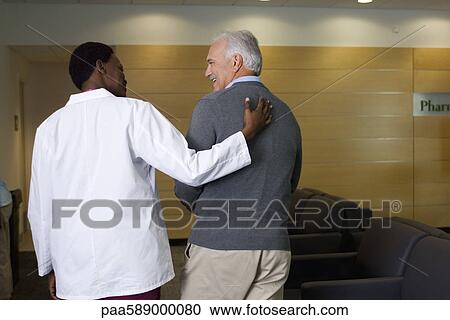 Stock Image - Doctor walking and talking with patient. Fotosearch
