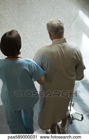 Stock Image - Nurse helping patient walk down hospital corridor. Fotosearch