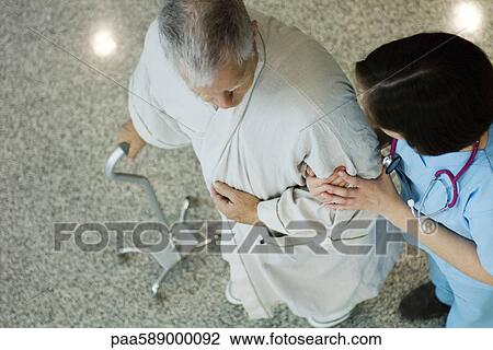 Nurse helping senior patient walk in corridor View Large Photo Image Stock Image - Nurse helping senior patient walk in corridor. Fotosearch