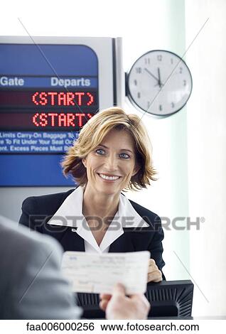 Stock Photograph - Airline attendant smiling at passenger at check-in counter. Fotosearch