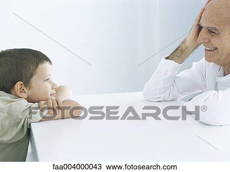 Boy and grandfather sitting across table, smiling at each other View Large Photo Image Stock Image - Boy and grandfather sitting across table, smiling at each other. Fotosearch
