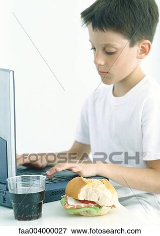 Boy having lunch while using laptop View Large Photo Image Stock Photo - Boy having lunch while using laptop. Fotosearch