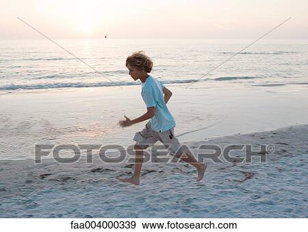 Stock Photo - Boy running on beach at sunset. Fotosearch