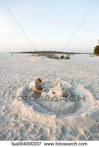 Stock Photo - Boy sitting next to sand castle on beach. Fotosearch