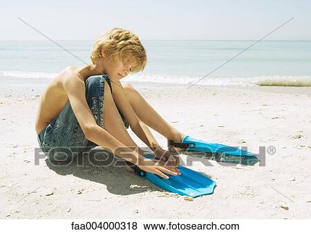 Boy sitting on beach, putting on flippers View Large Photo Image Stock Photo - Boy sitting on beach, putting on flippers. Fotosearch