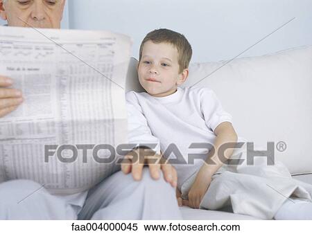 Boy sitting on sofa next to grandfather while he reads newspaper View Large Photo Image Stock Photography - Boy sitting on sofa next to grandfather while he reads newspaper. Fotosearch