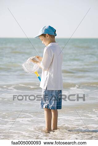 Stock Image - Boy standing in sea holding fishing net. Fotosearch