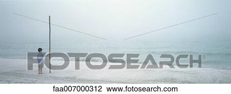 Boy standing on beach, holding onto tall pole View Large Photo Image Stock Image - Boy standing on beach, holding onto tall pole. Fotosearch