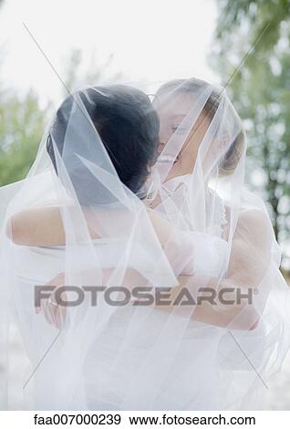 Stock Photo - Bride and groom embracing under veil. Fotosearch