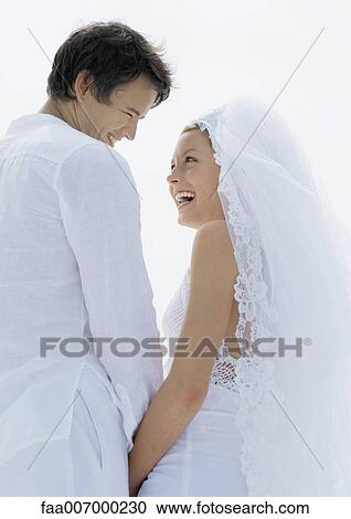 Stock Image - Bride and groom smiling at each other, low angle view. Fotosearch