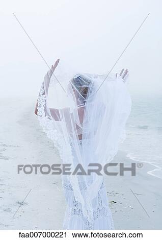 Stock Image - Bride holding up veil on beach. Fotosearch