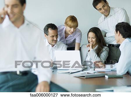 Stock Photo - Business colleagues gathered around laptop, smiling. Fotosearch