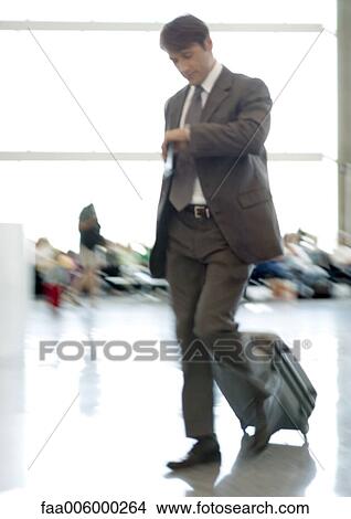 Picture - Businessman checking watch as he walks through airport, blurred motion. Fotosearch