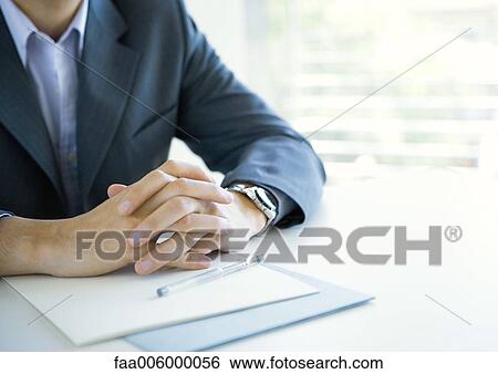 Businessman clasping hands on desk, cropped View Large Photo Image Stock Photograph - Businessman clasping hands on desk, cropped. Fotosearch