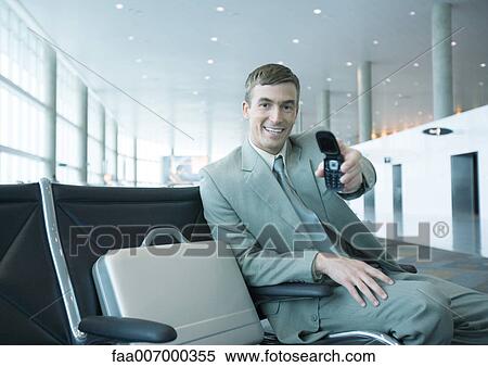 Businessman holding out cell phone in airport lounge View Large Photo Image Stock Photography - Businessman holding out cell phone in airport lounge. Fotosearch