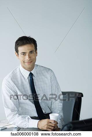 Stock Photo - Businessman in office, holding cup and smiling at camera. Fotosearch