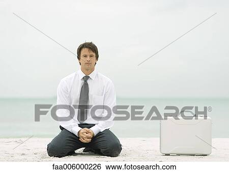Businessman kneeling on beach next to briefcase View Large Photo Image Stock Photograph - Businessman kneeling on beach next to briefcase. Fotosearch
