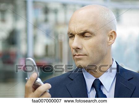 Stock Photo - Businessman looking at cell phone, furrowing brow. Fotosearch