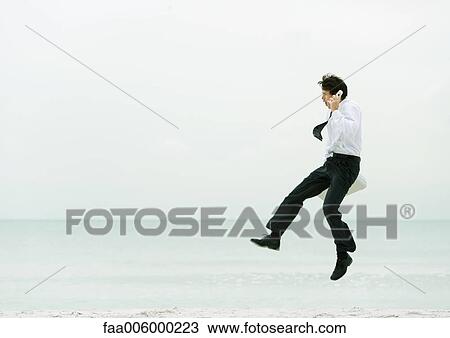 Businessman on beach, using cell phone and jumping View Large Photo Image Stock Image - Businessman on beach, using cell phone and jumping. Fotosearch
