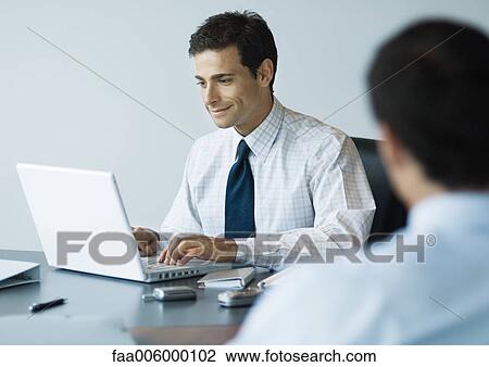 Stock Image - Businessman sitting at desk using laptop. Fotosearch