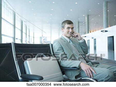 Picture - Businessman sitting in airport lounge, using cell phone. Fotosearch