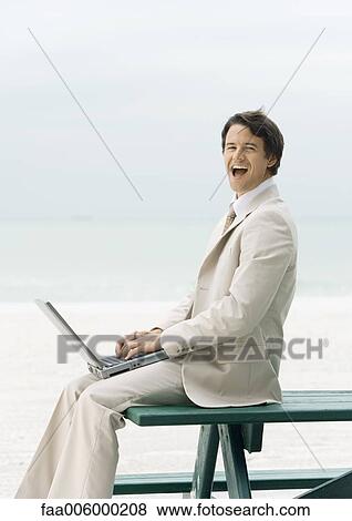 Businessman sitting on edge of picnic table at beach, using laptop View Large Photo Image Stock Photo - Businessman sitting on edge of picnic table at beach, using laptop. Fotosearch