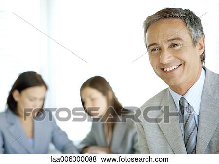 Stock Photo - Businessman smiling, colleagues in background. Fotosearch