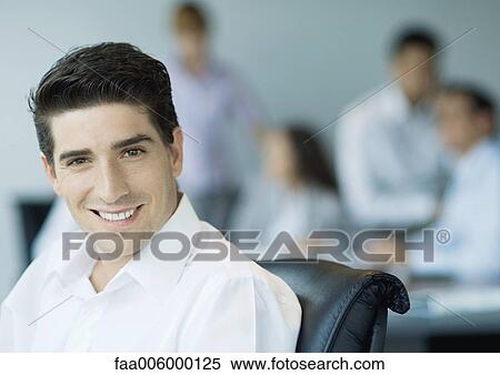 Businessman smiling, colleagues in background View Large Photo Image Stock Photography - Businessman smiling, colleagues in background. Fotosearch